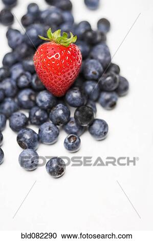 Stock Image - Strawberry on pile of blueberries. Fotosearch