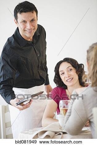Stock Photo - Waiter bring check to customers at table in restaurant. Fotosearch