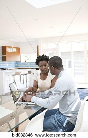 Stock Photograph - Black couple using laptop together in kitchen. Fotosearch