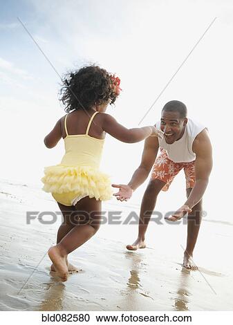 Black father bending to greet daughter on beach View Large Photo Image Stock Image - Black father bending to greet daughter on beach. Fotosearch