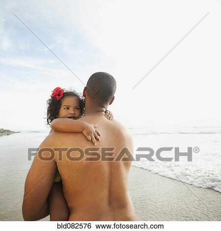 Stock Photograph - Black father carrying daughter on beach. Fotosearch