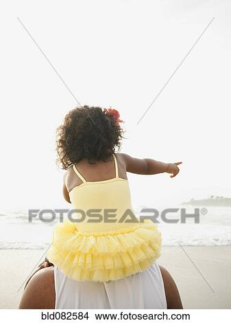 Picture - Black father carrying daughter on shoulders at beach. Fotosearch