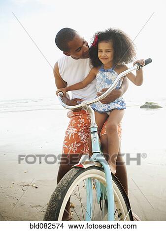 Black father helping daughter learn to ride retro bicycle View Large Photo Image Picture - Black father helping daughter learn to ride retro bicycle. Fotosearch