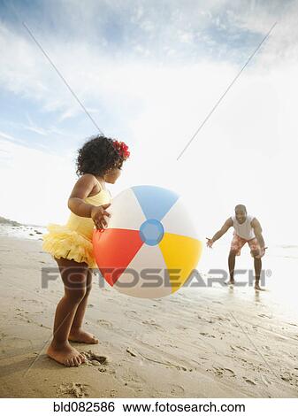 Stock Photograph - Black father throwing ball on beach with daughter. Fotosearch