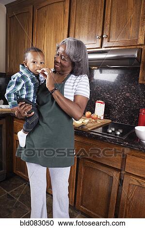 Stock Image - Black grandmother feeding grandson in kitchen. Fotosearch