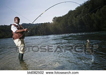 Stock Image - Black man catching fish in stream. Fotosearch