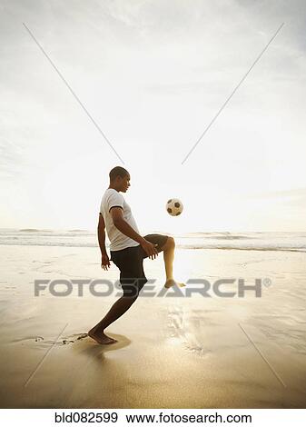 Stock Photo - Black man playing with soccer ball on beach. Fotosearch