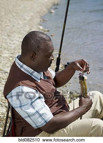 Stock Image - Black man removing fish from hook near stream. Fotosearch