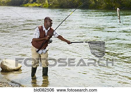 Stock Photograph - Black man with net catching fish in stream. Fotosearch