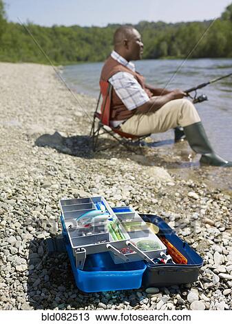 Stock Image - Black man with tackle box fishing in stream. Fotosearch