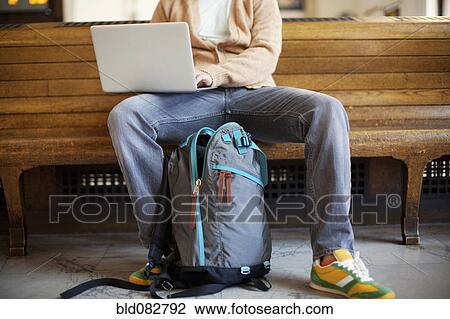 Stock Image - Caucasian man sitting on bench using laptop. Fotosearch