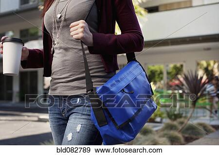 Stock Photo - Caucasian woman walking with messenger bag and coffee. Fotosearch