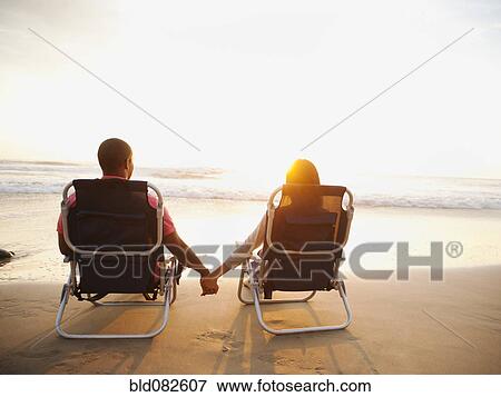 Stock Photo - Couple holding hands on beach at sunset. Fotosearch