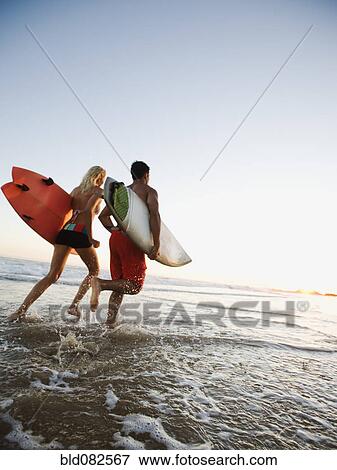 Couple running on beach carrying surfboards View Large Photo Image Stock Photo - Couple running on beach carrying surfboards. Fotosearch