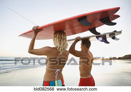 Stock Photo - Couple walking on beach carrying surfboards. Fotosearch