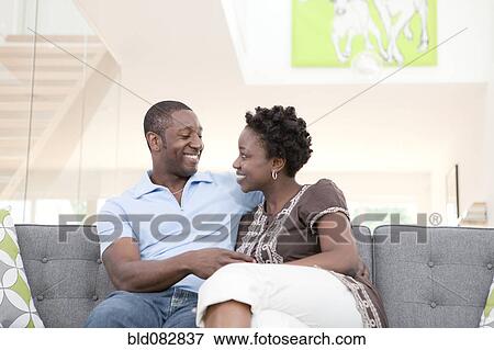 Stock Photo - Happy couple sitting on sofa in living room. Fotosearch