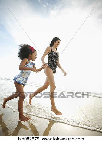 Stock Photo - Hispanic mother and daughter holding hands and walking on beach. Fotosearch