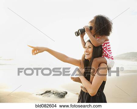 Picture - Hispanic mother carrying daughter with binoculars on beach. Fotosearch