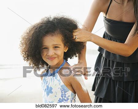 Stock Photo - Hispanic mother rubbing sunscreen on daughter at beach. Fotosearch