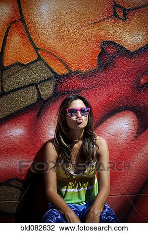 Stock Image - Hispanic woman standing near graffiti wall making face. Fotosearch