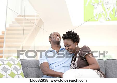 Stock Photo - Laughing couple sitting on sofa in living room. Fotosearch