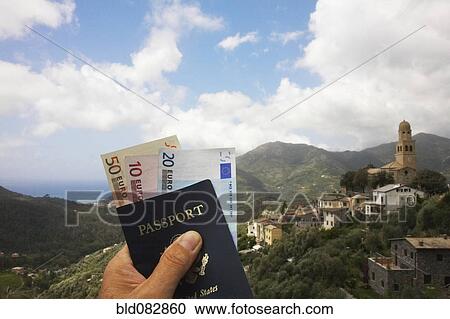 Stock Image - Manís hand holding passport and euro currency. Fotosearch