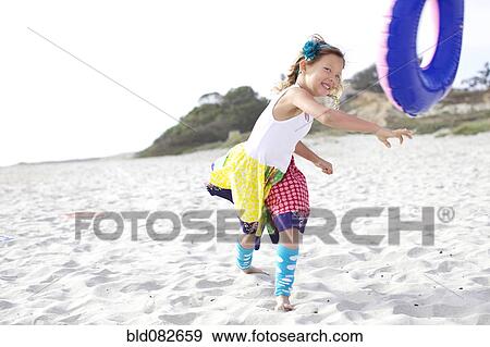 Stock Photo - Mixed race girl playing with inflatable ring on beach. Fotosearch