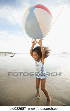 Stock Photo - Mixed race girl playing with large ball on beach. Fotosearch