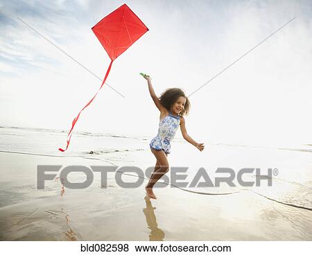 Stock Photo - Mixed race girl running with kite on beach. Fotosearch