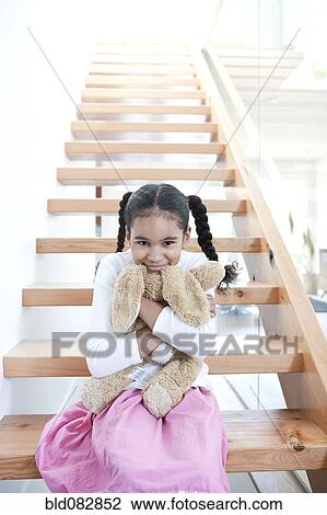 Stock Image - Mixed race girl sitting on steps with stuffed animal. Fotosearch