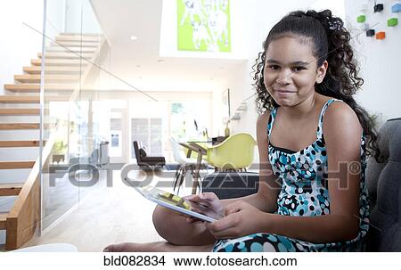 Picture - Mixed race girl using digital tablet in living room. Fotosearch