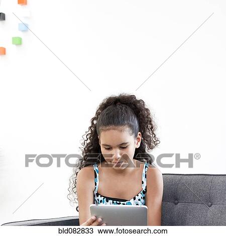 Stock Image - Mixed race girl using digital tablet in living room. Fotosearch