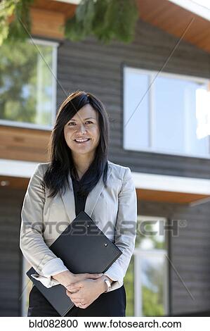 Stock Image - Mixed race real estate agent standing near house. Fotosearch