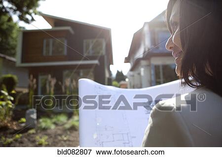 Stock Photo - Mixed race real estate agent standing near house reviewing blueprints. Fotosearch