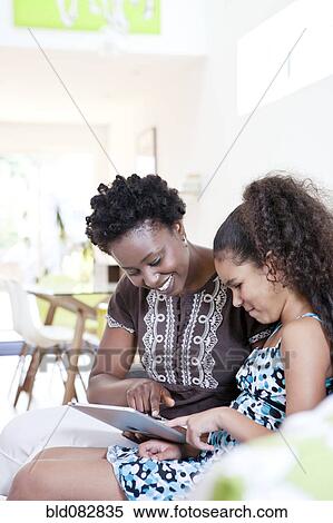 Mother and daughter using digital tablet in living room View Large Photo Image Stock Photography - Mother and daughter using digital tablet in living room. Fotosearch