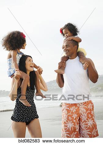 Stock Image - Parents carrying children on shoulders at beach. Fotosearch