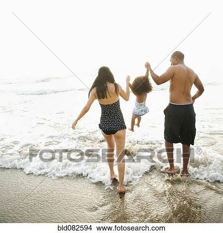 Picture - Parents swinging daughter between them on beach. Fotosearch