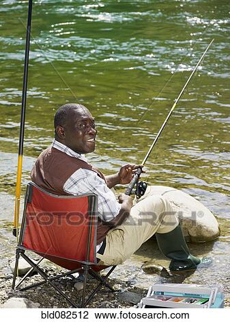Stock Image - Smiling Black man fishing in stream. Fotosearch