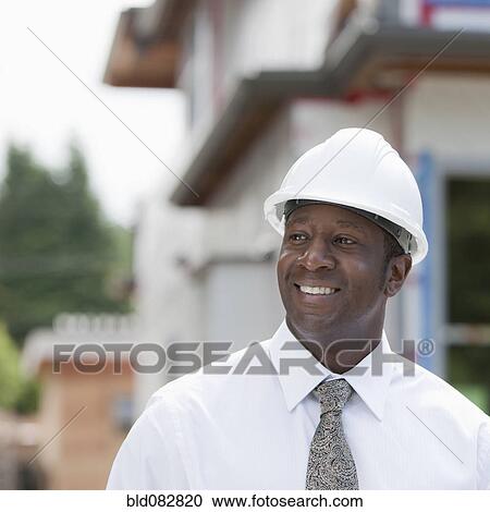 Stock Image - Smiling Black real estate agent in hard-hat near construction site. Fotosearch