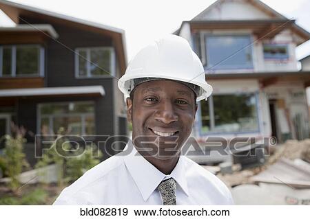 Stock Photo - Smiling Black real estate agent in hard-hat near construction site. Fotosearch