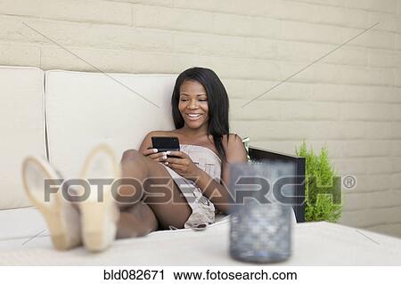 Smiling Black woman text messaging on bed View Large Photo Image Stock Image - Smiling Black woman text messaging on bed. Fotosearch
