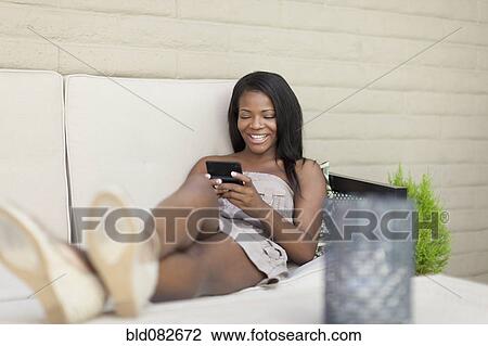 Smiling Black woman text messaging on bed View Large Photo Image Stock Image - Smiling Black woman text messaging on bed. Fotosearch