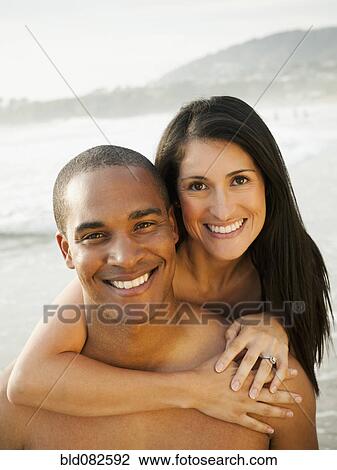 Stock Image - Smiling couple hugging on beach. Fotosearch