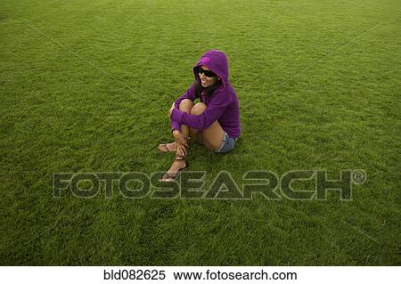 Stock Photography - Smiling Hispanic woman sitting in grass. Fotosearch