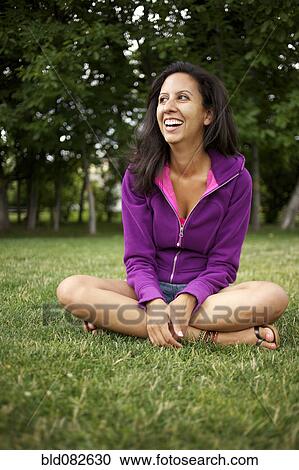 Stock Image - Smiling Hispanic woman sitting in park. Fotosearch