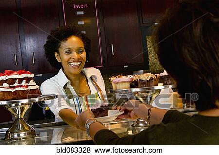 Stock Photo - African American bakery owner serving customer cupcake. Fotosearch