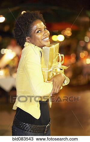 Stock Image - African American woman hugging gift at night. Fotosearch