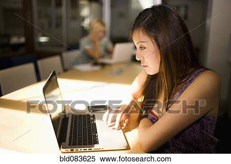 Stock Photography - Asian businesswoman using laptop in communal workspace. Fotosearch