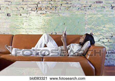 Stock Image - Black woman using digital table on sofa in living room. Fotosearch