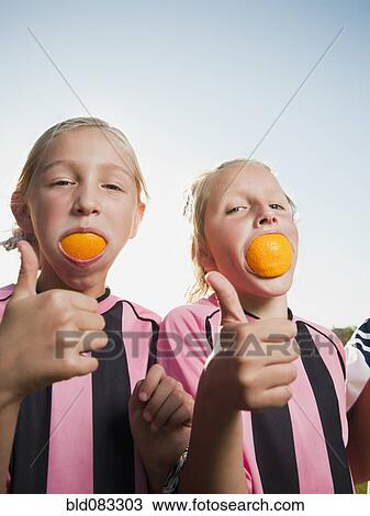 Stock Image - Caucasian girl soccer players eating orange slices. Fotosearch